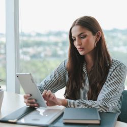 Confident businesswoman using a tablet while sitting at a desk in a modern office setting.