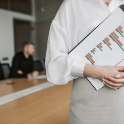 Close-up of a person holding a clipboard with charts in a meeting room.